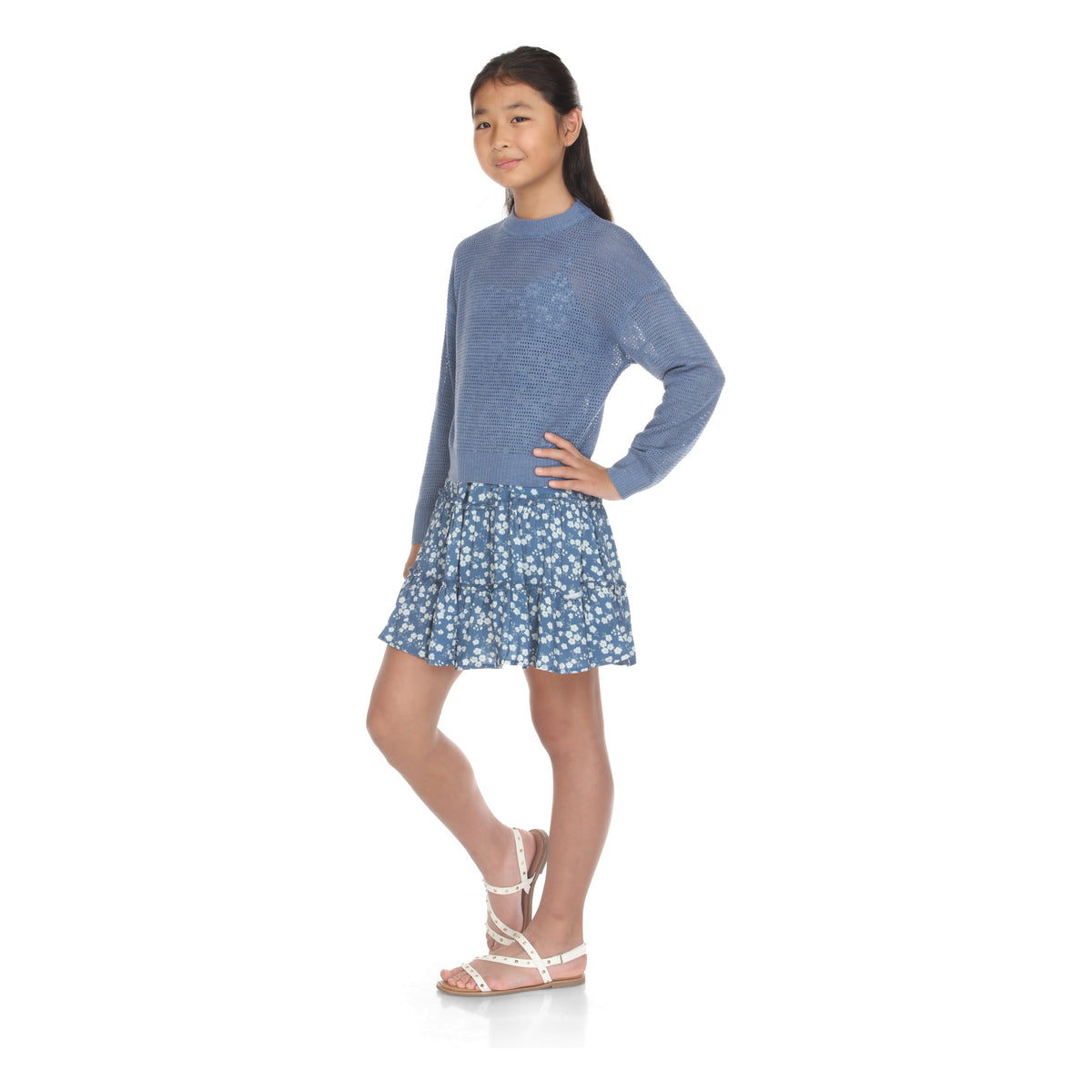 Model wears the blue open-knit sweater and blue floral tiered dress set, hand on hip, front view