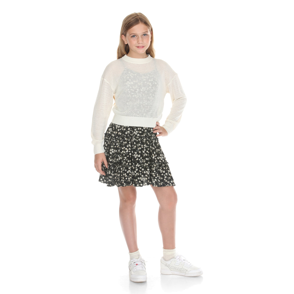 Model wears the ivory open-knit sweater and black floral tiered dress set, hand on hip, front view
